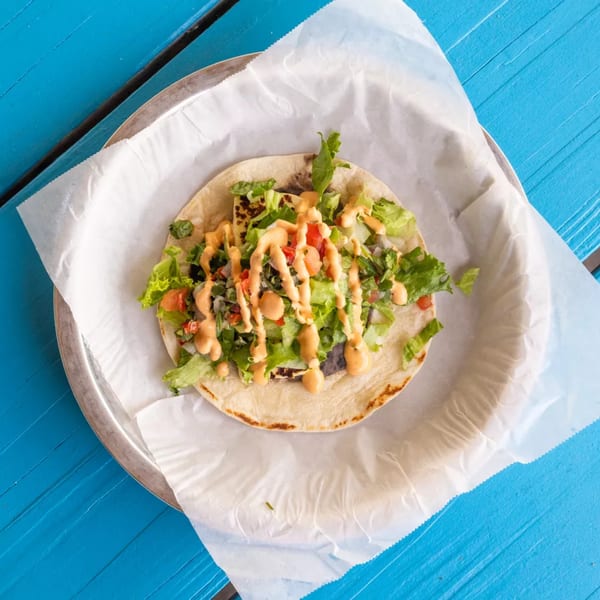 A grilled halloumi taco with lettuce, salsa, and chipotle aioli on a blue wooden table.