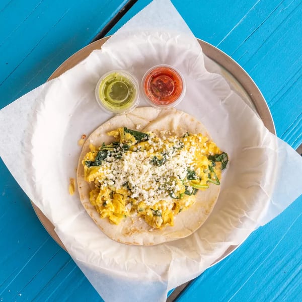 Scrambled egg and spinach taco with crumbled cheese, served with green and red salsa.