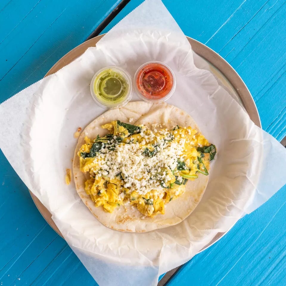 Scrambled egg and spinach taco with crumbled cheese, served with green and red salsa.