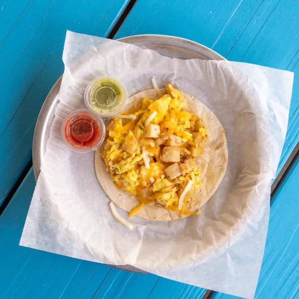 Breakfast taco with scrambled eggs, potatoes, cheese, and two sauces on a blue wooden table.