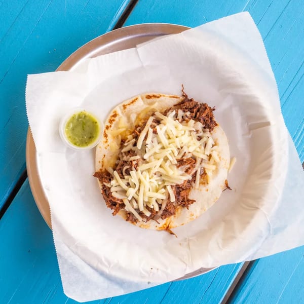 Overhead view of a single taco with shredded meat and cheese, with a side of green salsa.
