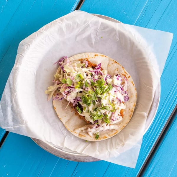 Overhead view of a fish taco with white and purple cabbage slaw and cilantro on a blue wooden table.