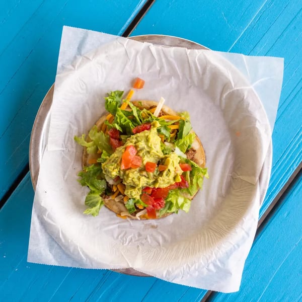 Overhead view of a tostada topped with ground beef, lettuce, cheese, tomatoes, and guacamole.