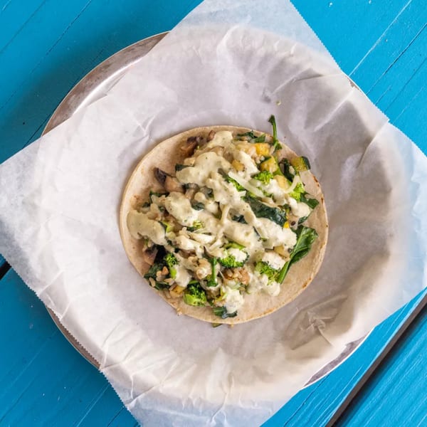 A veggie taco with broccoli, spinach, and a creamy sauce, served on parchment paper.