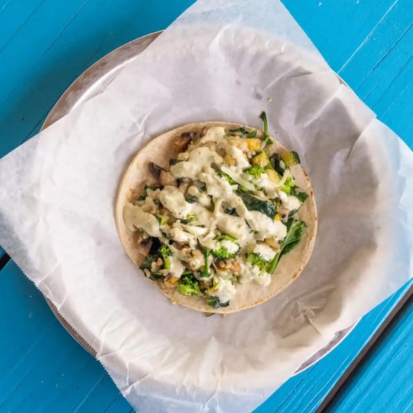 A single taco filled with broccoli, spinach, and other vegetables, drizzled with white sauce.
