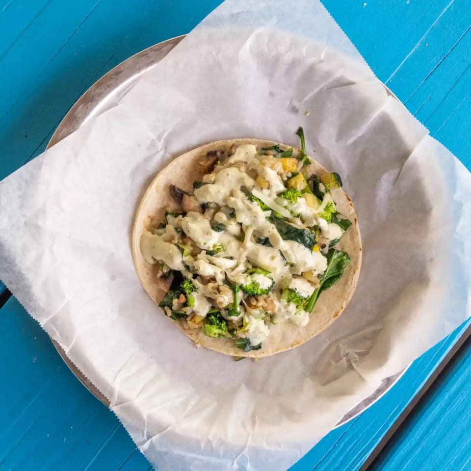 A single taco filled with broccoli, spinach, and other vegetables, drizzled with white sauce.