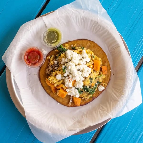 Breakfast tostada with scrambled eggs, spinach, sweet potatoes, and feta cheese, with two sauces.