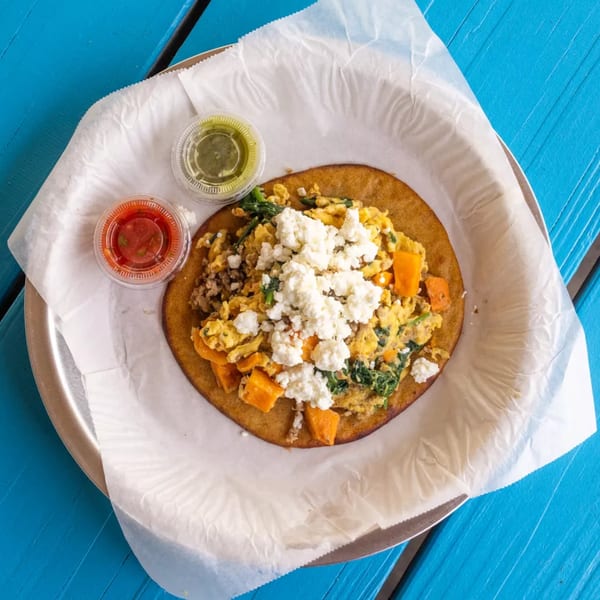 Breakfast tostada with scrambled eggs, sweet potatoes, spinach, and feta cheese, with two sauces.